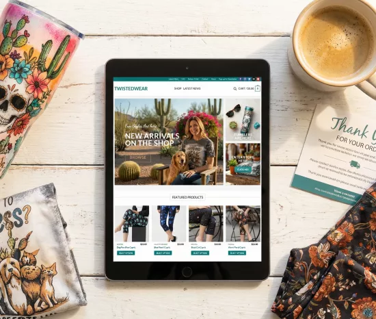 Custom WooCommerce website design for a handmade apparel and tumbler brand, displayed on a tablet amidst products.